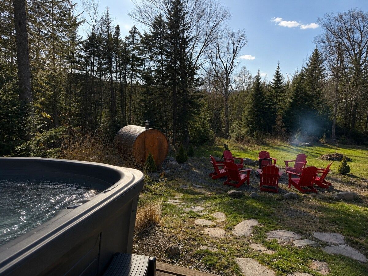 The hot tub at dusk with the fire pit and red Muskoka chairs beyond