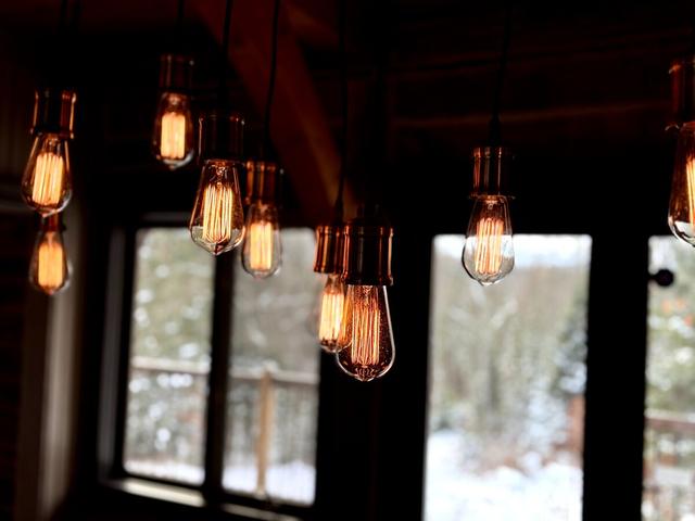 Edison-bulb pendants over the dining table with the forest in the window behind