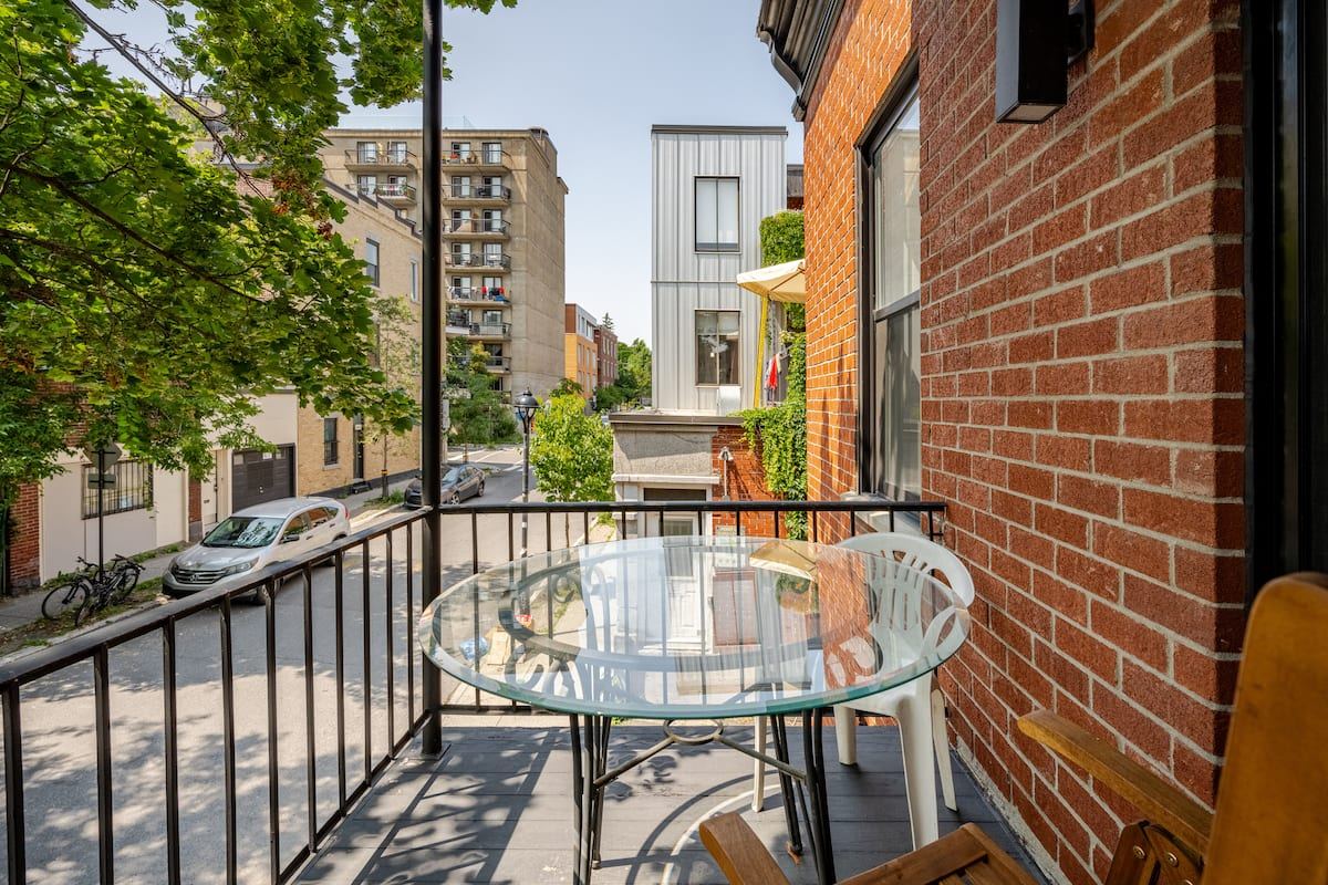 The front balcony with a glass table, red brick, and the tree-lined street below