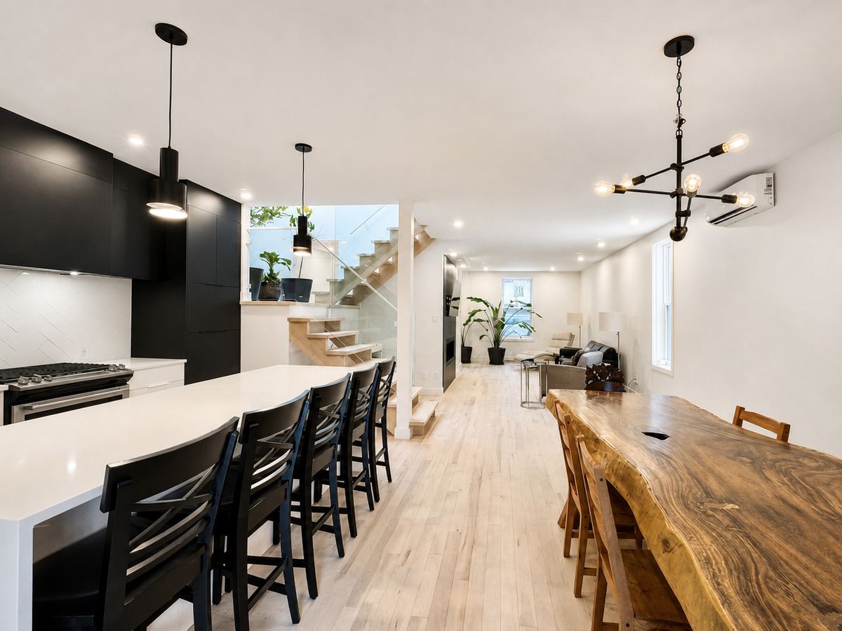 The open-plan main floor of the Plateau house: white kitchen, live-edge table, floating staircase