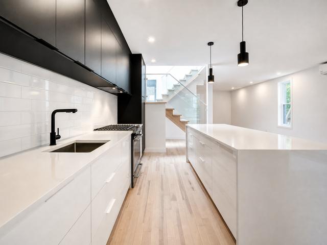 The galley kitchen with white counters, black upper cabinets and pendant lights