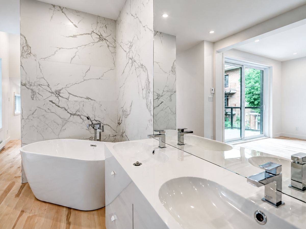 Freestanding white tub against a marble wall, white vanity beside it