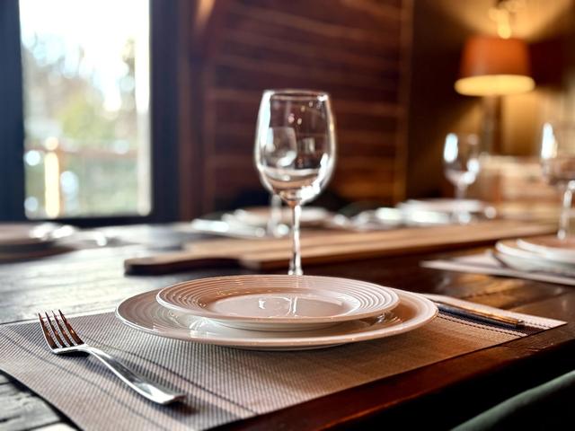 A place setting with wine glass at the dining table, the forest in the window